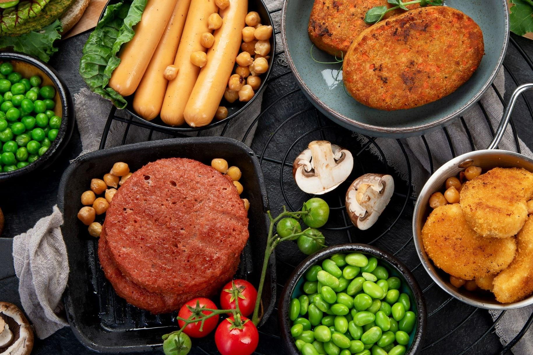 Ein Tisch voll Alternativer Proteine: Hülsenfrüchte, Pilze, Würstchen und Schnitzel aus Fleischersatz.