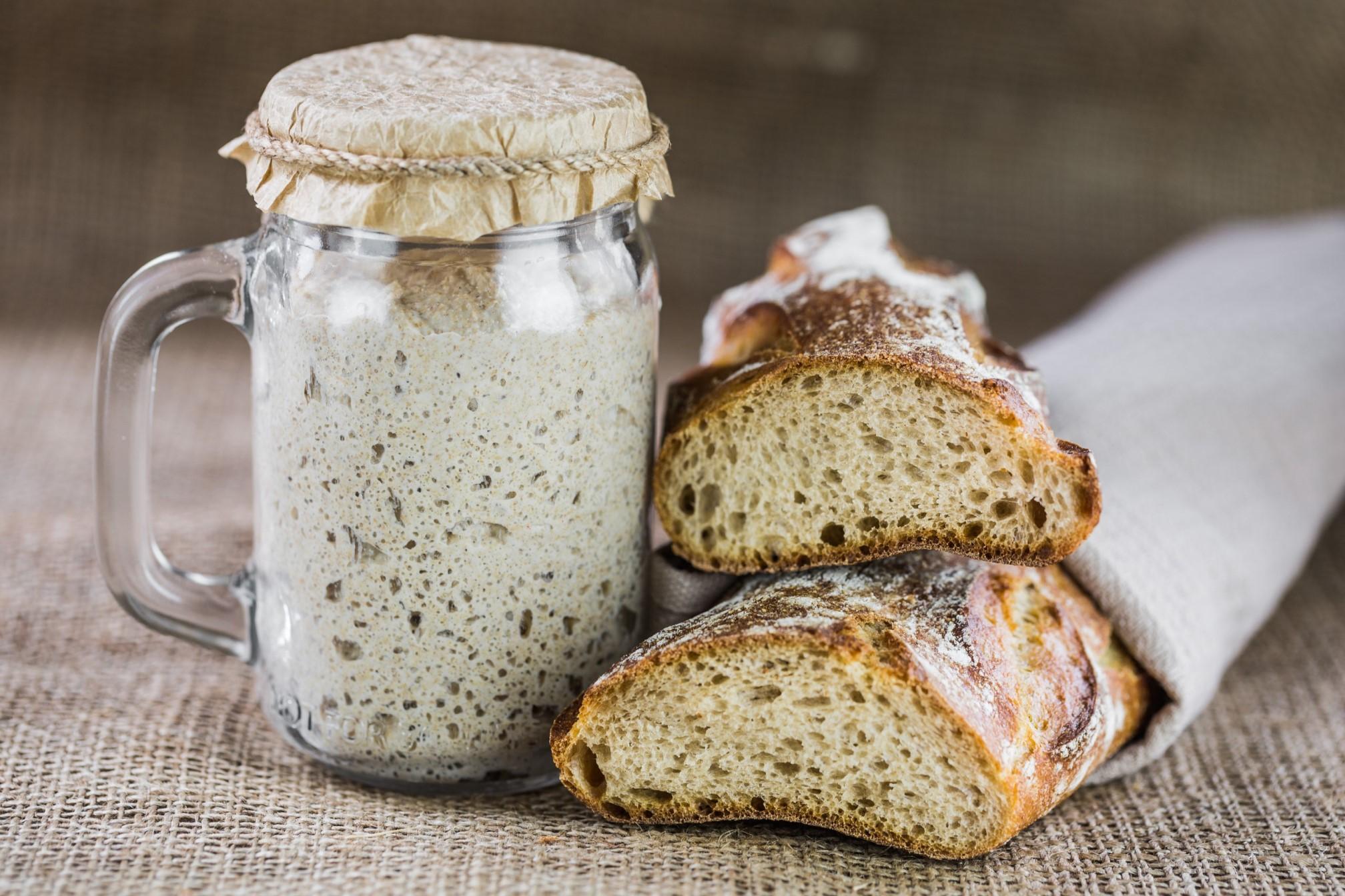 Ein Glas mit Sauerteig steht neben einem angeschnittenen Sauerteigbrot
