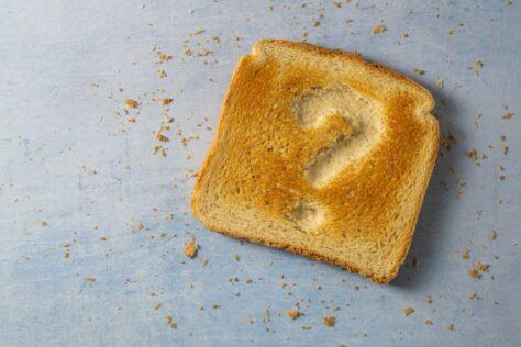 Geröstete Toastbrotscheibe mit eingedrücktem Fragezeichen auf blauem Untergrund