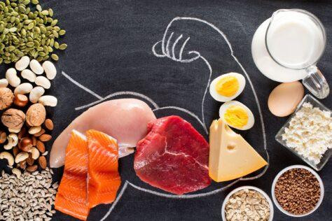 Verschiedene proteinreiche Lebensmittel vor schwarzem Hintergrund, auf den der Umriss eines muskulösen Arms gezeichnet wurde